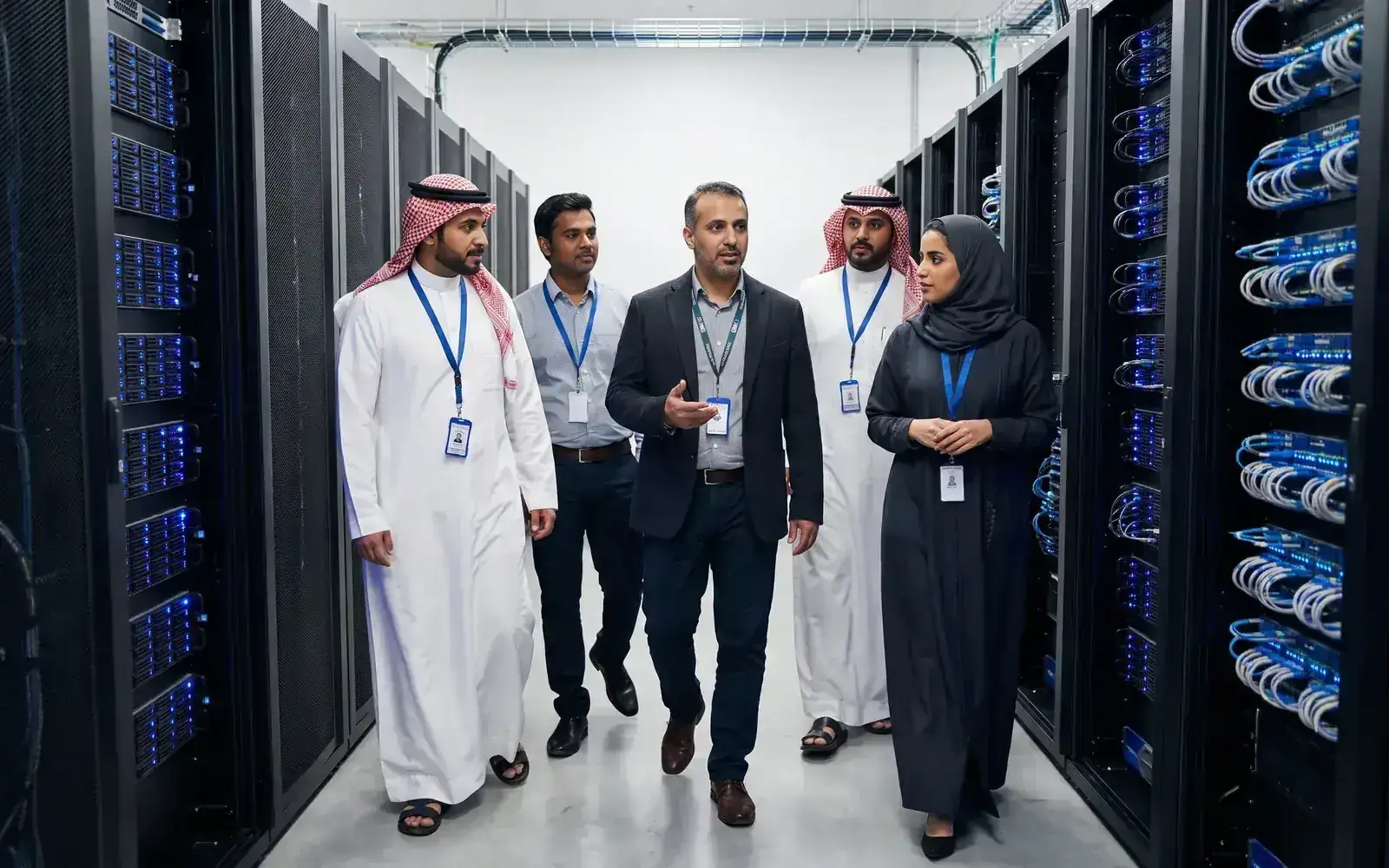 A CTO and four colleagues wearing lanyards walk along an aisle of server racks in a data centre